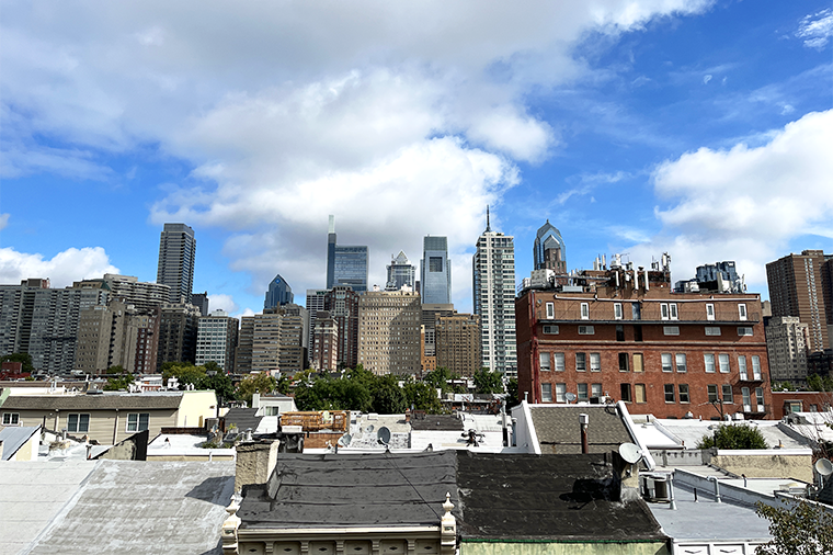 A photo of the Philadelphia skyline set against a bright blue sky and big white clouds