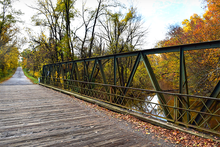 A photo of a wood bridge connecting a trail over water in the fall