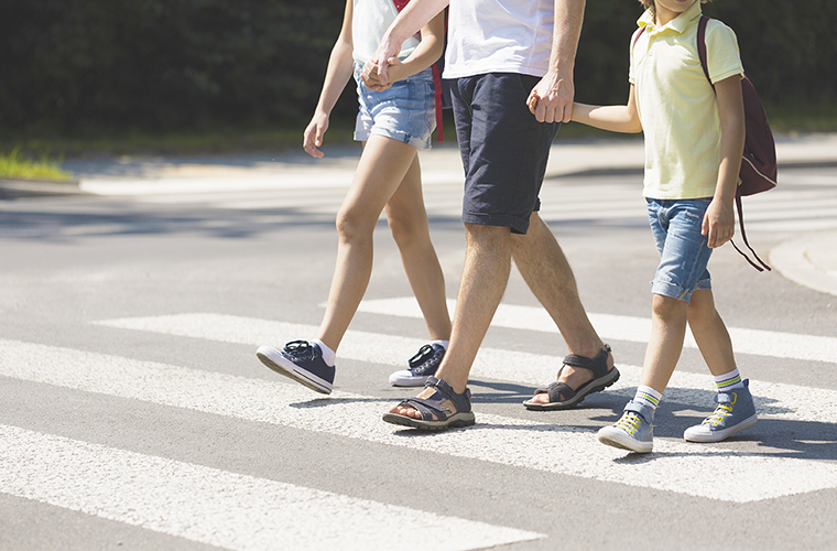 A photo of an adult walking with two children in a crosswalk