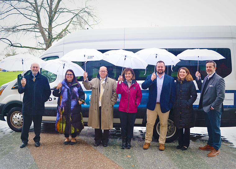 A photo of people holding umbrellas standing in front of the autonomous vehicle shuttle in Philadelphia's Navy Yard