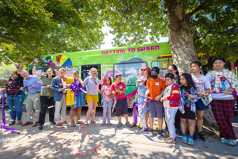 A photo of adults and children celebrating a ribbon cutting in front of a SEPTA bus wrapped in artwork