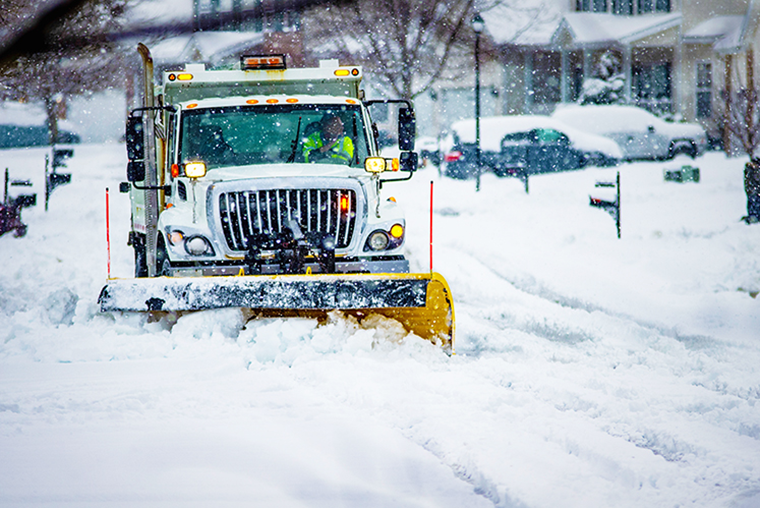 A snow plow plows a snow-covered residential road